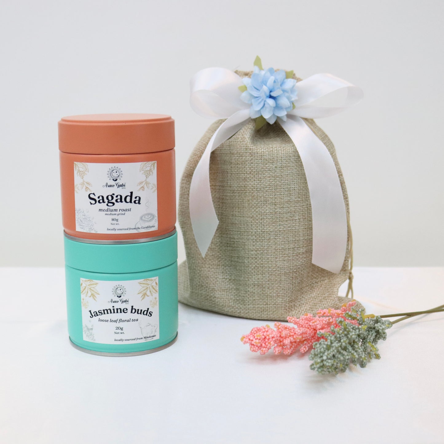 sagda coffee grounds and jasmine buds loose leaf tea in tin cans beside a burlap pouch