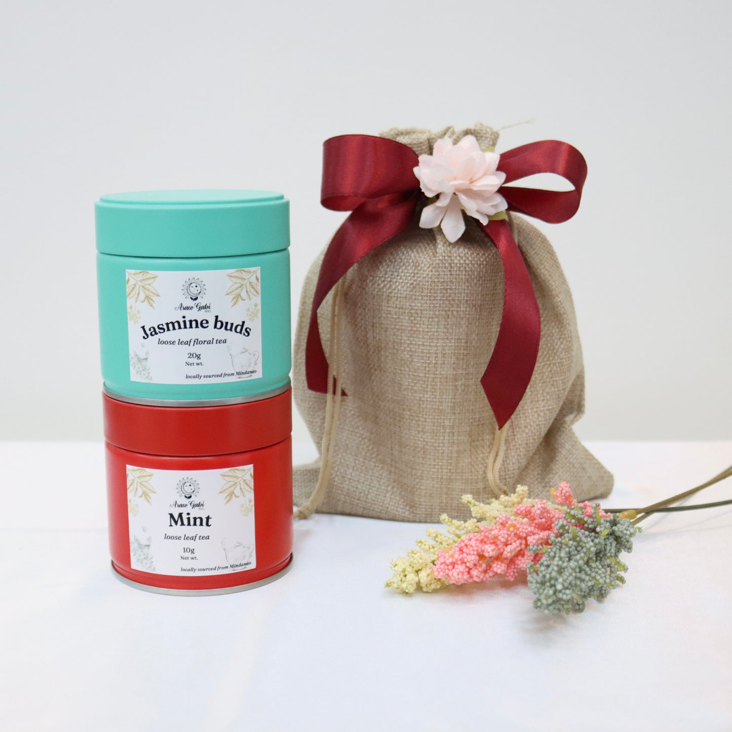 jasmine buds and mint loose leaf tea in tin cans beside a burlap pouch